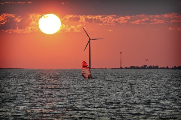 Kuva surffaajasta auringonlaskussa, tuulivoimala taustalla