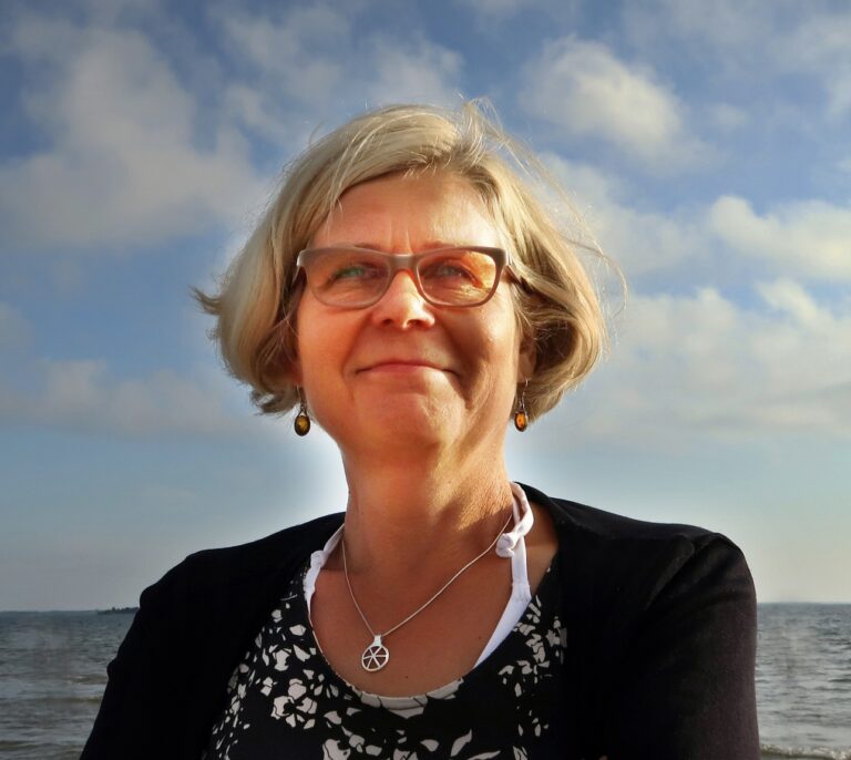 Liisa Nummelin kuvassa ulkona. Taustalla sininen taivas ja pilviä.