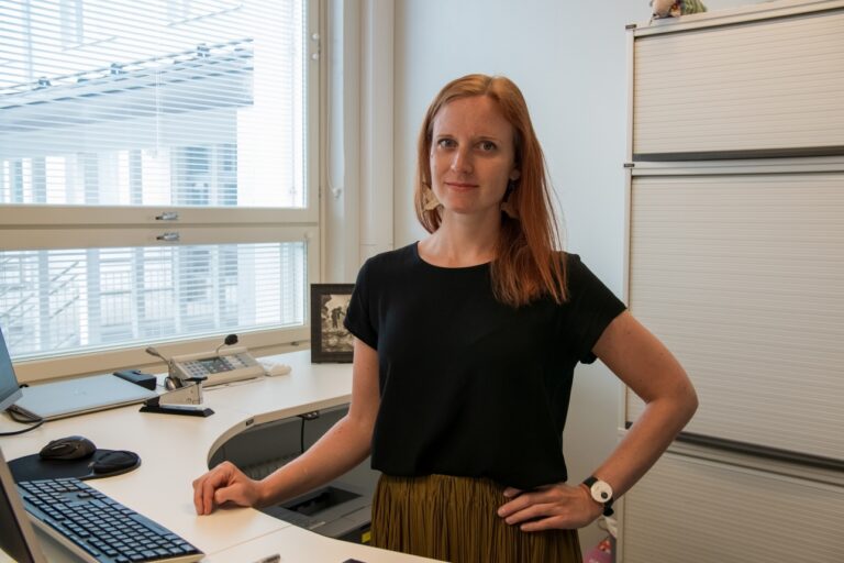 Veera Toivonen seisoo kuvassa työpöytänsä ääressä
