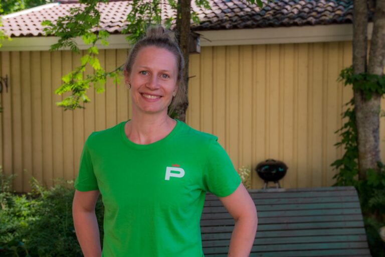 Nainen hymyilee vihreässä t-paidassa puun alla kesällä, rintakuva