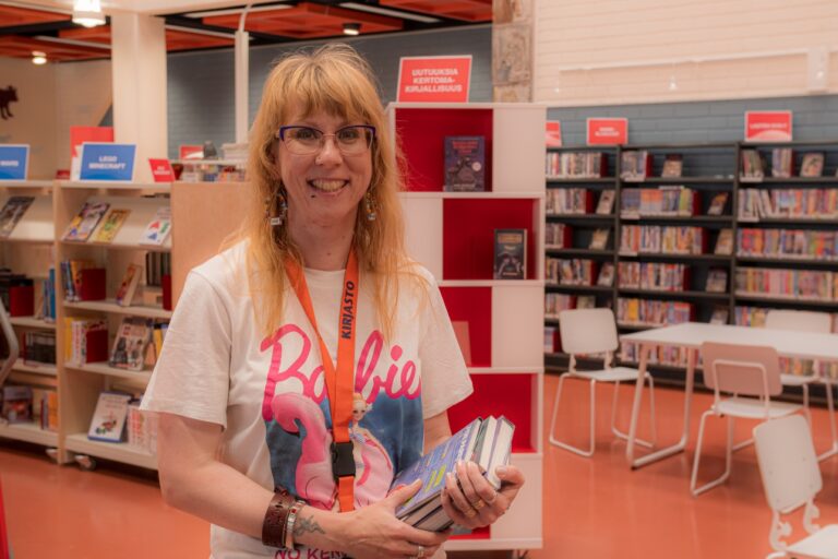 Arja Palonen kirjastossa, kädessään kirjoja