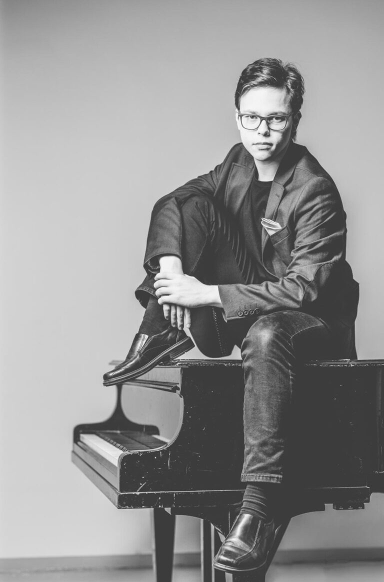 Tarmo Peltokoski istuu mustavalkokuvassa flyygelin päällä.