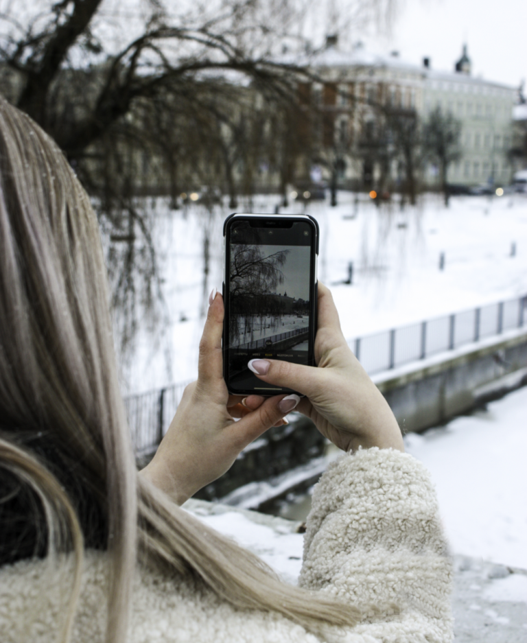 Henkilö ottamassa puhelimella kuvaa lumisesta maisemasta