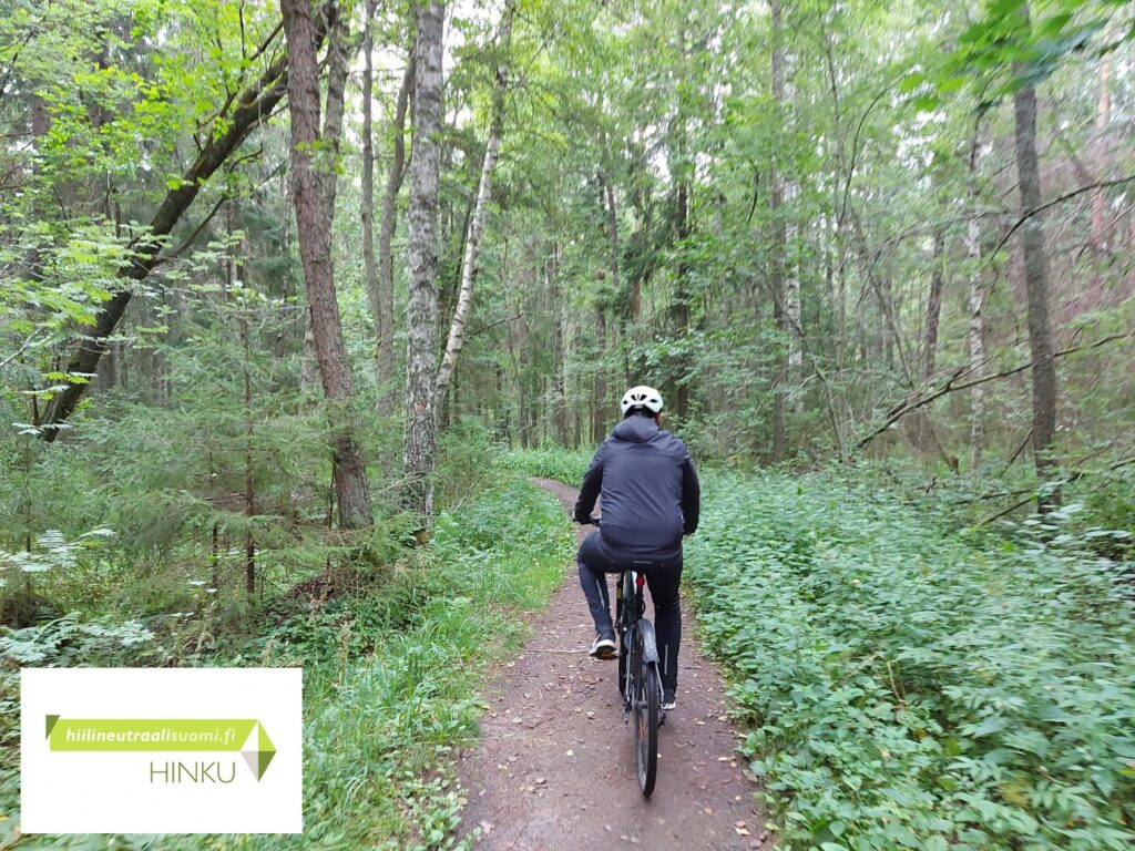 pyöräilijä vihreässä metsässä, hinku logo alhaalla vasemmalla