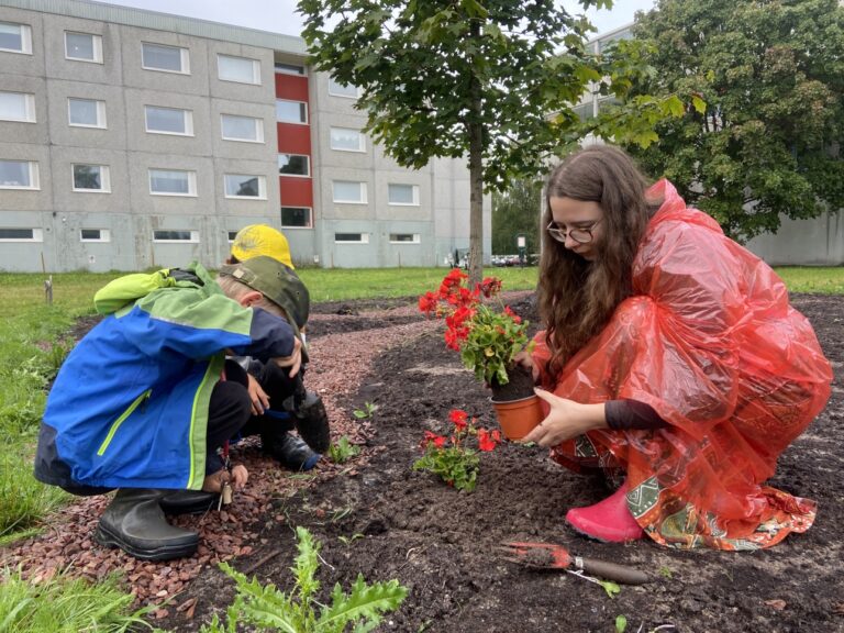 Lapset ja nainen istuttavat kukkia Growing Canvas -taideteokseen Väinölässä
