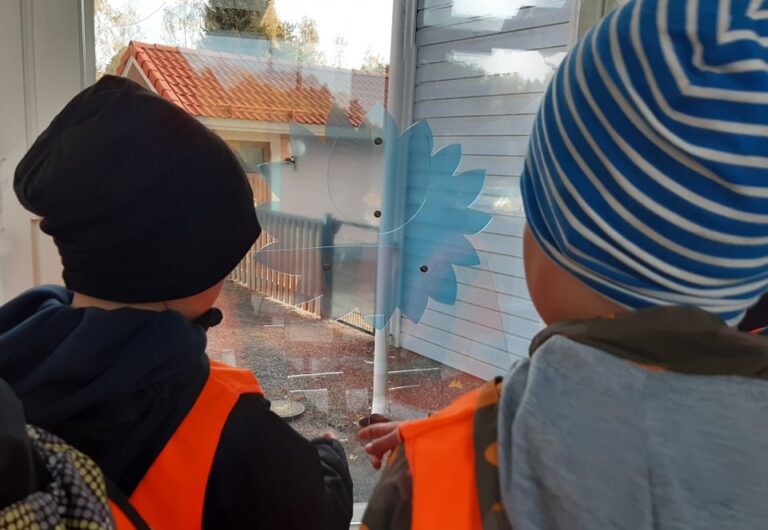 Kaksi lasta katsovat ikkunan edessä olevaa taideteosta, sisäkuva.