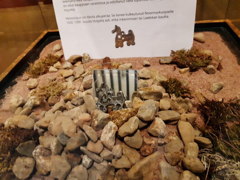 Metalllinen hevosen tyylinen esine, joka lepää kivien päällä lasisella kuvulla päällystetyssä kuutiossa.