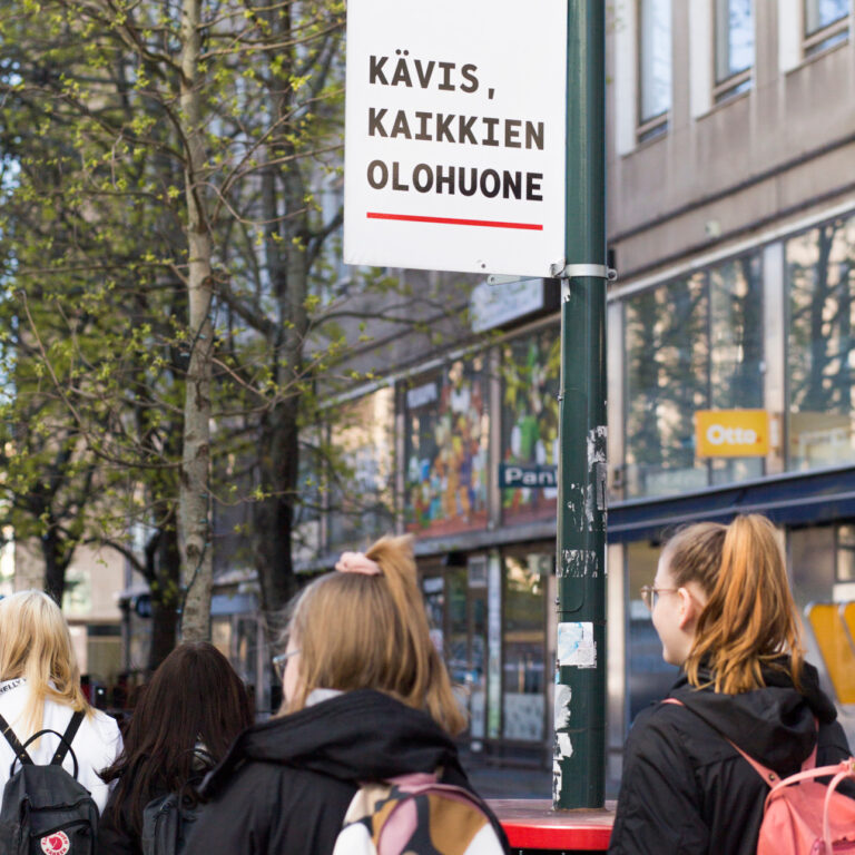 Nuoria kävelemässä ja yläpuolella kyltti Kävis, kaikkien olohuone