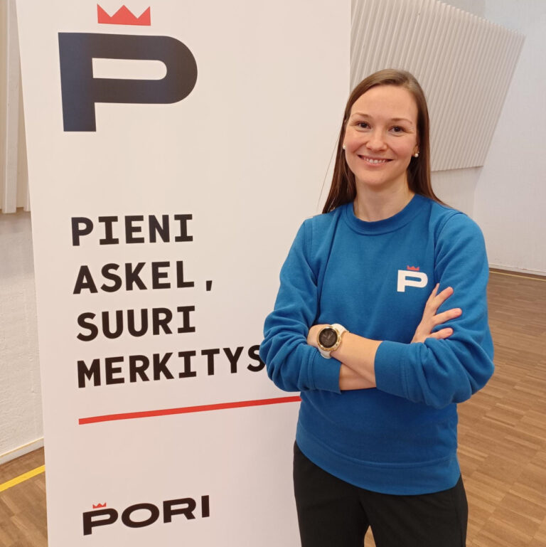 Sinipaitainen nainen seisoo Pori-esitteen edessä, esitteessä lukee pieni askel, suuri merkitys