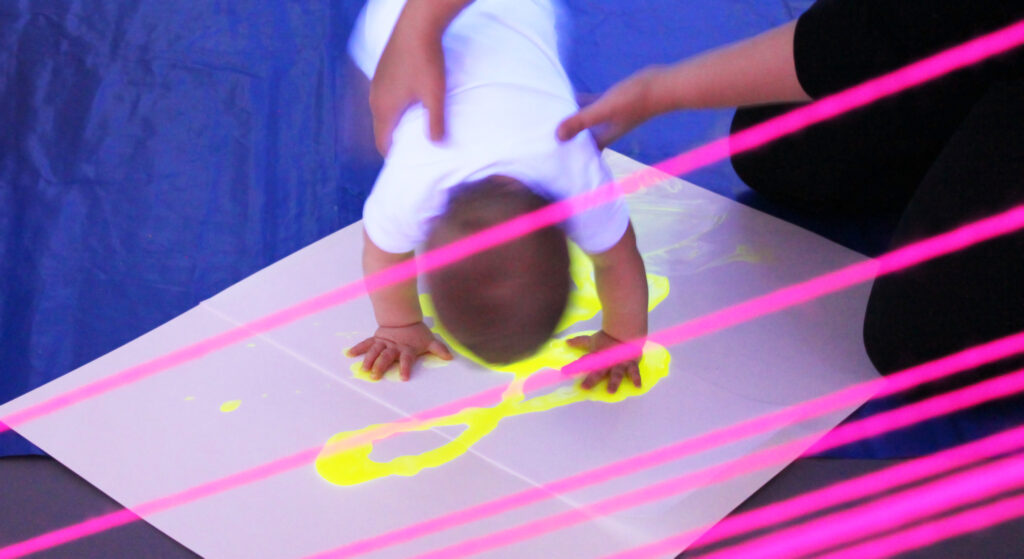 A baby is painting with their hands and an adult is supporting their posture.