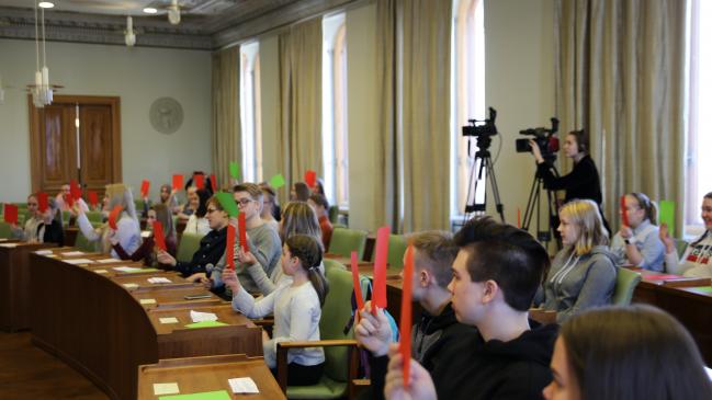 Kuvassa on nuoria, jotka pitävät kädessää eri värisiä papereita.