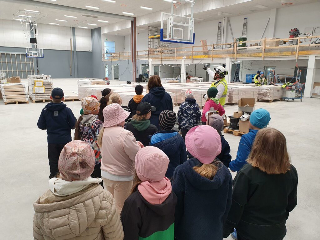 Etualalla takaapäin oppilaita ja taustalla rakennustyömaan seiniä
