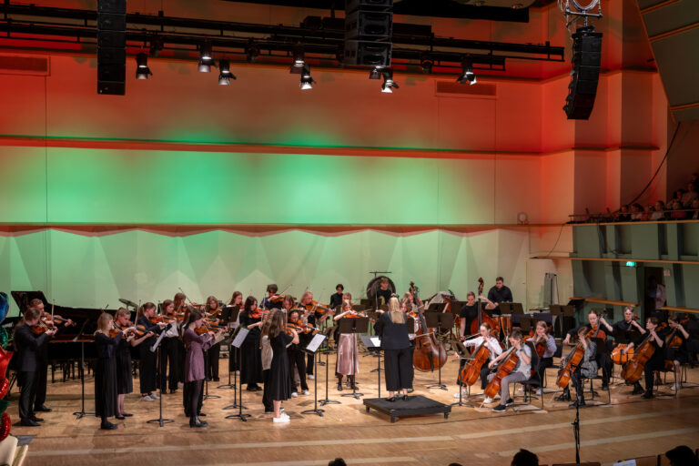 Kuva konserttisalista, jossa lavalla nuoria jousisoittajia.