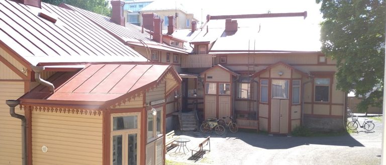 Kuvassa puisia vaaleita vanhoja rakennuksia Mikonkadun ja Katariinankadun kulmassa, jossa yhdistykset jakavat pihapiirin.