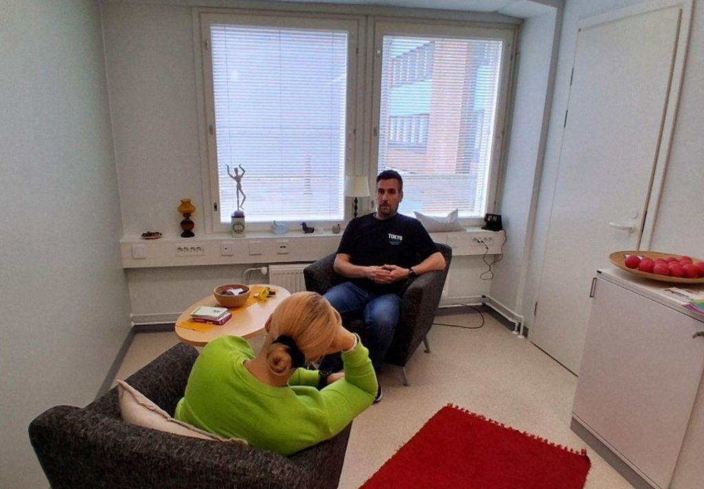 Vaaleassa huoneessa ikkunan edessä kaksi ihmistä istumassa tuoleilla ja keskustelemassa.