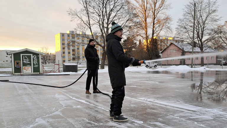 Kaksi miestä jäädyttämättä Käppärän luistelukenttää