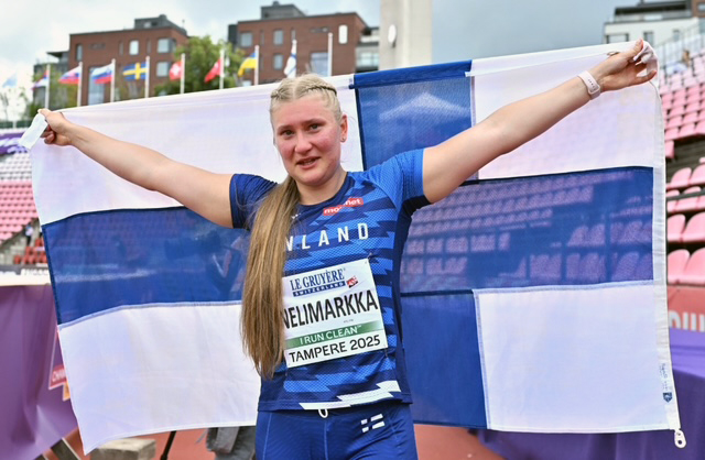 Keihäänheittäjä Rebecca Nelimarkka seisoo stadionilla ja pitää käsissään suurta Suomen lippua levitettynä selkänsä takana.