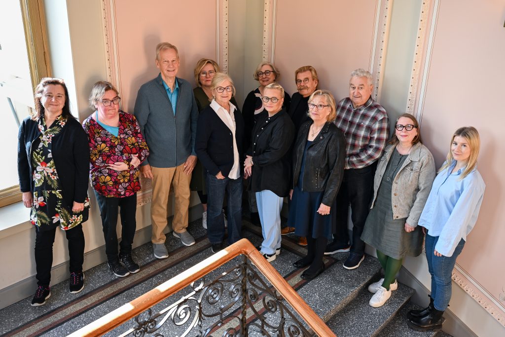 Seniorineuvoston jäsenet seisomassa Porin kaupungintalon koristeellisessa portaikossa ja hymyilemässä kameraan.