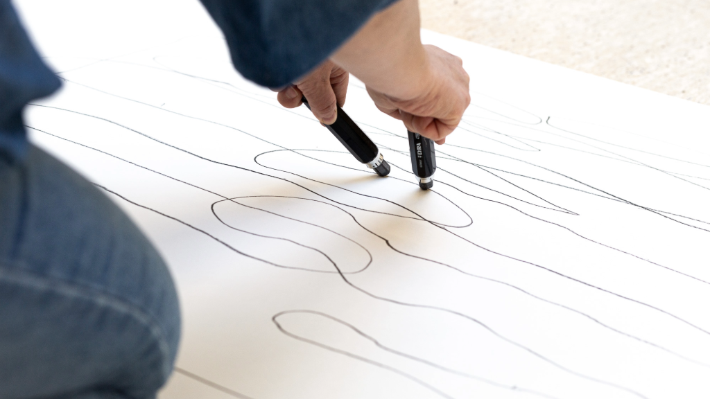 Kaksi kättä piirtää mustia viivoja paperille