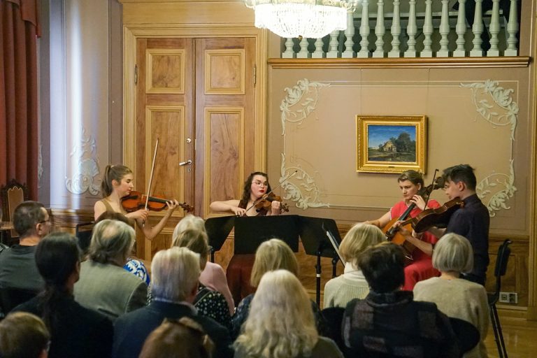 Konserttikuva vuoden 2025 seniorien kulttuuriviikon tapahtumasta, jossa Pori Sinfoniettan jousikvartetti esiintyy Porin Raatihuoneen juhlasalissa järjestetyssä kamarikonsertissa. Jousikvartetin lisäksi kuvassa näkyy konserttiin osallistunutta yleisöä.