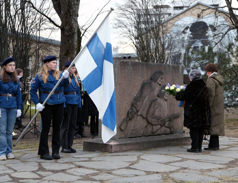 Tapahtumakuva Porissa vuonna 2025 järjestetystä talvisodan päättymisen muistopäivän tilaisuudesta. Etualalla näkyy partiolaisten lippuvartio, johon kuuluu Suomen lipunkantaja ja kaksi vartijaa. Taustalla näkyy Summan taistelun muistomerkki, johon on kaiverrettu kaksi sotilashahmoa. Muistomerkin edessä kaksi henkilöä asettaa kukkalaitetta sen juurelle.