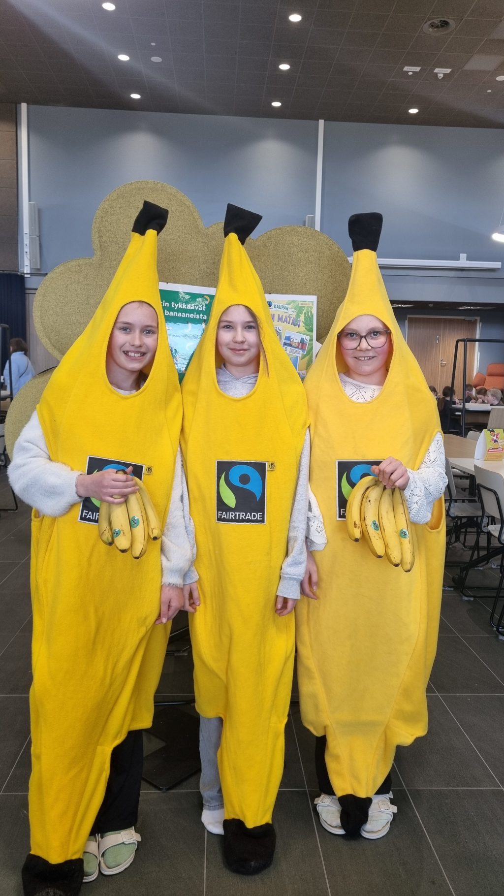 Kolme banaaniasuihin pukeutunulla lasta pitelee käsissään banaaneja