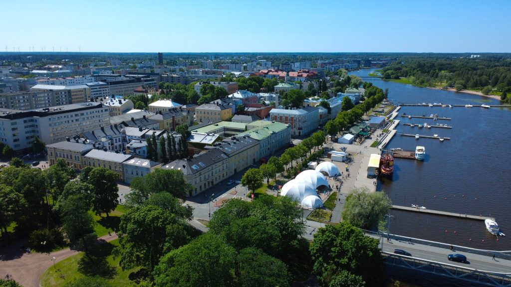 Ilmakuva Etelärannasta, oikealla puolella Kokemäenjoki, etualalla kirkkopuiston puita ja taustalla taloja. Kuvassa myös valkeakupolinen Etelärannan SuomiAreena-lava.