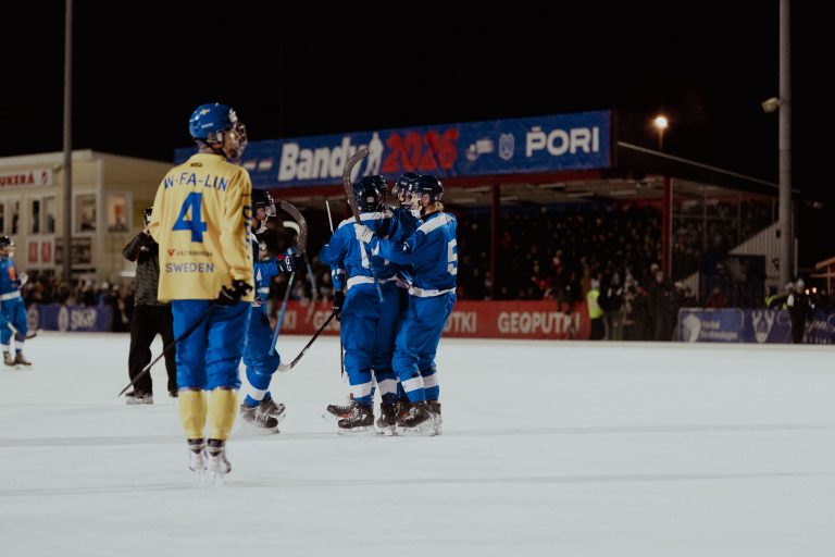 Jäällä keltapaitainen Ruotsin pelaaja ja sinipaitaisia Suomen pelaajia