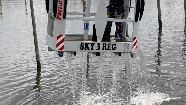 Kuvassa nosturin kori jossa haalaripukeinen opiskelija kastautuu jokiveteen.