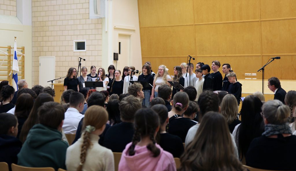 Kuva vuoden 2025 kansallisen veteraanipäivän juhlan musiikkiesityksestä, jossa Porin Lyseon koulun musiikkiluokan kuoro esiintyy runsaslukuiselle yleisölle.