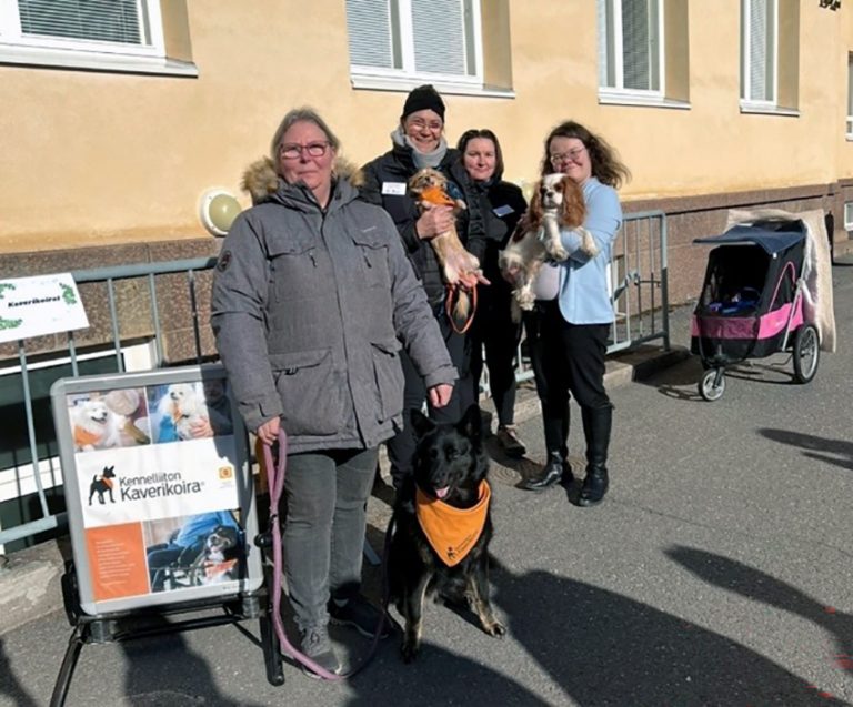 Neljä Kennelliiton kaverikoirien toiminnassa mukana olevaa henkilöä seisoo Porin lukion sisäpihalla koulurakennuksen seinustalla. Osalla heistä on koira sylissä tai he pitävät kiinni koiran talutushihnasta.