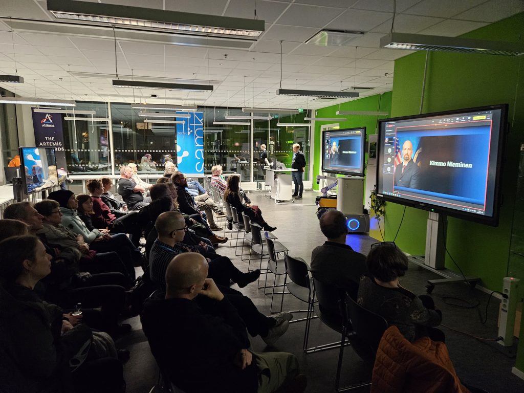 Samkissa kokoushuoneessa katsojia ja ruudulla kuva NASAn astronautti Kimmo Niemisestä.