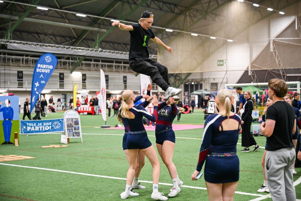 Mustiin pukeutuneita cheerleadereita joukossa ja yksi heistä hyppää